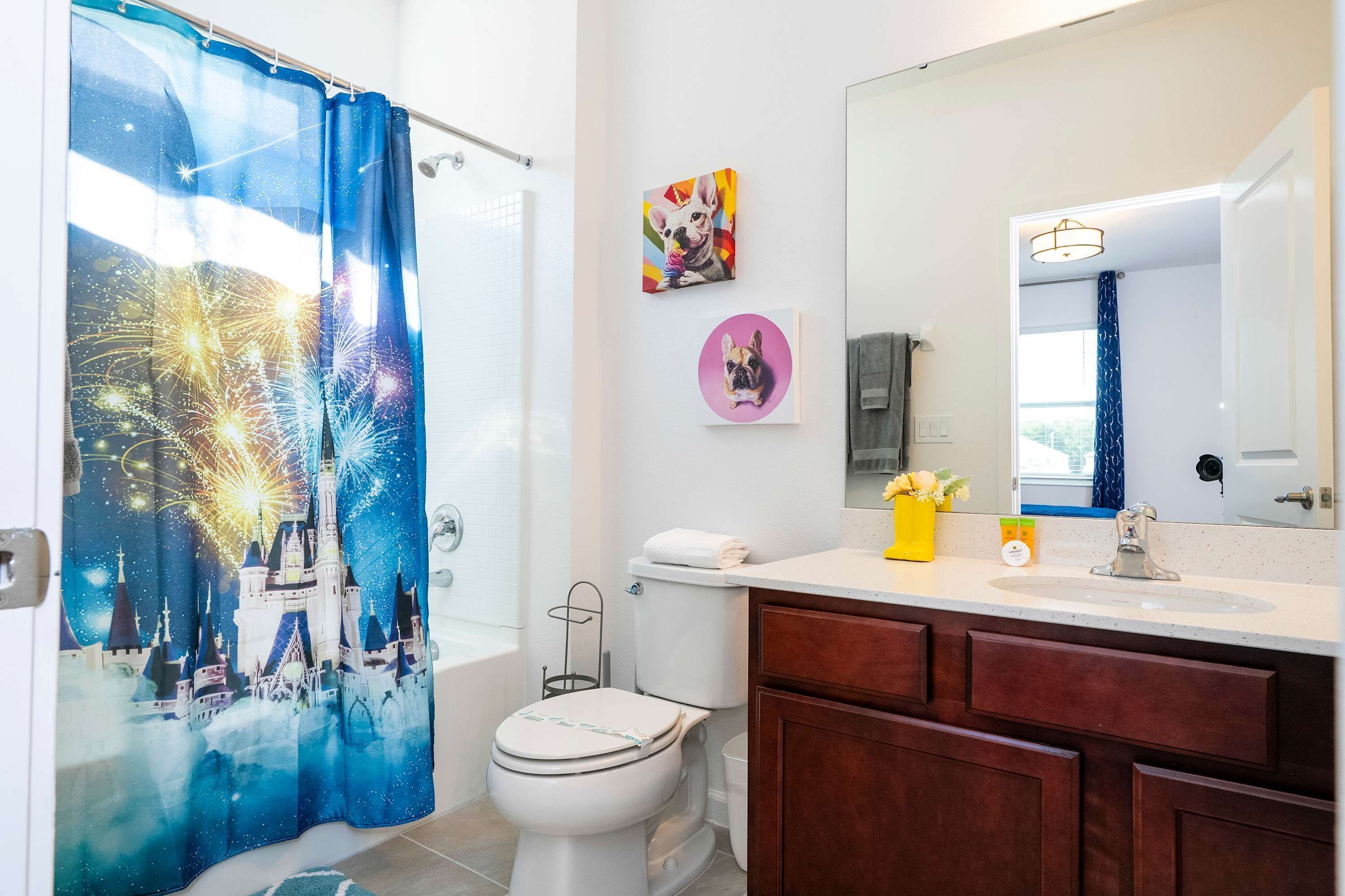 Baño con cortina de ducha que muestra fuegos artificiales y un castillo, un inodoro, un lavabo con espejo y un armario.