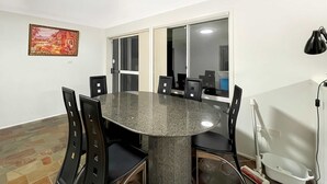 A conference room with a round table, black chairs, a painting on the wall, and a window with blinds.