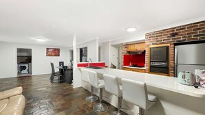 A modern kitchen with a central island, bar stools, a red accent wall, and a brick backsplash.