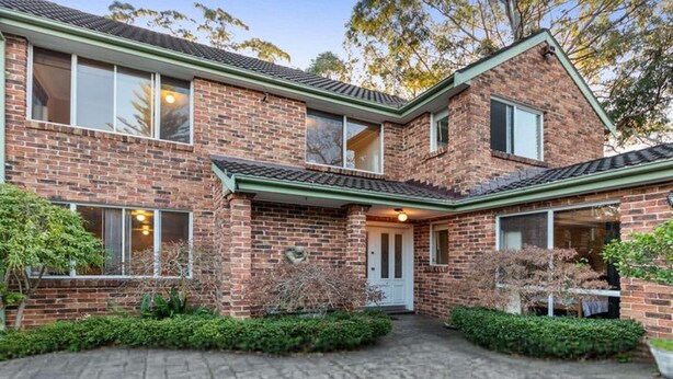A two-story brick house with a front porch, a covered driveway, and a small garden area.
