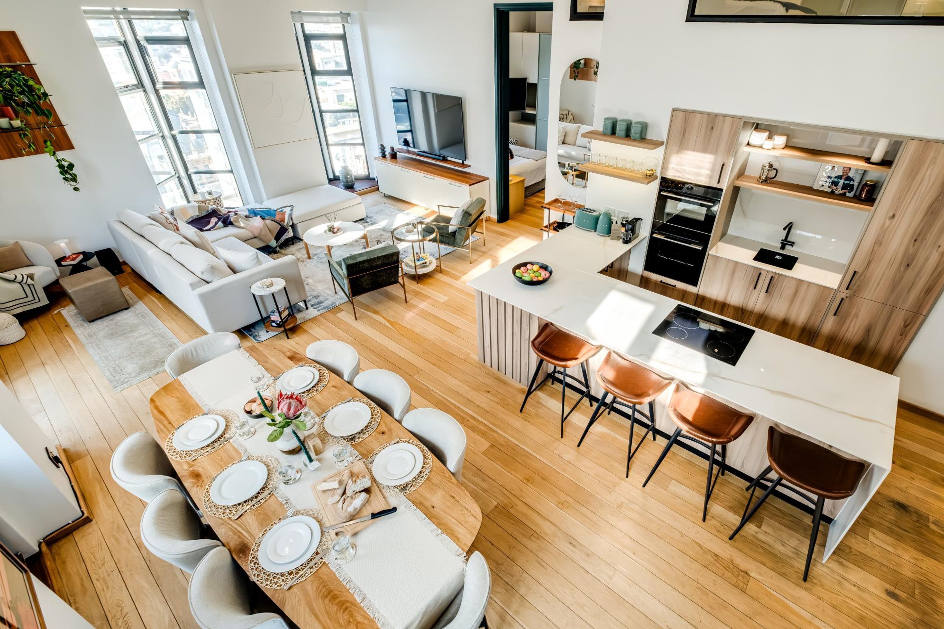A modern apartment with a dining area, kitchen, living room, and a large window providing natural light.