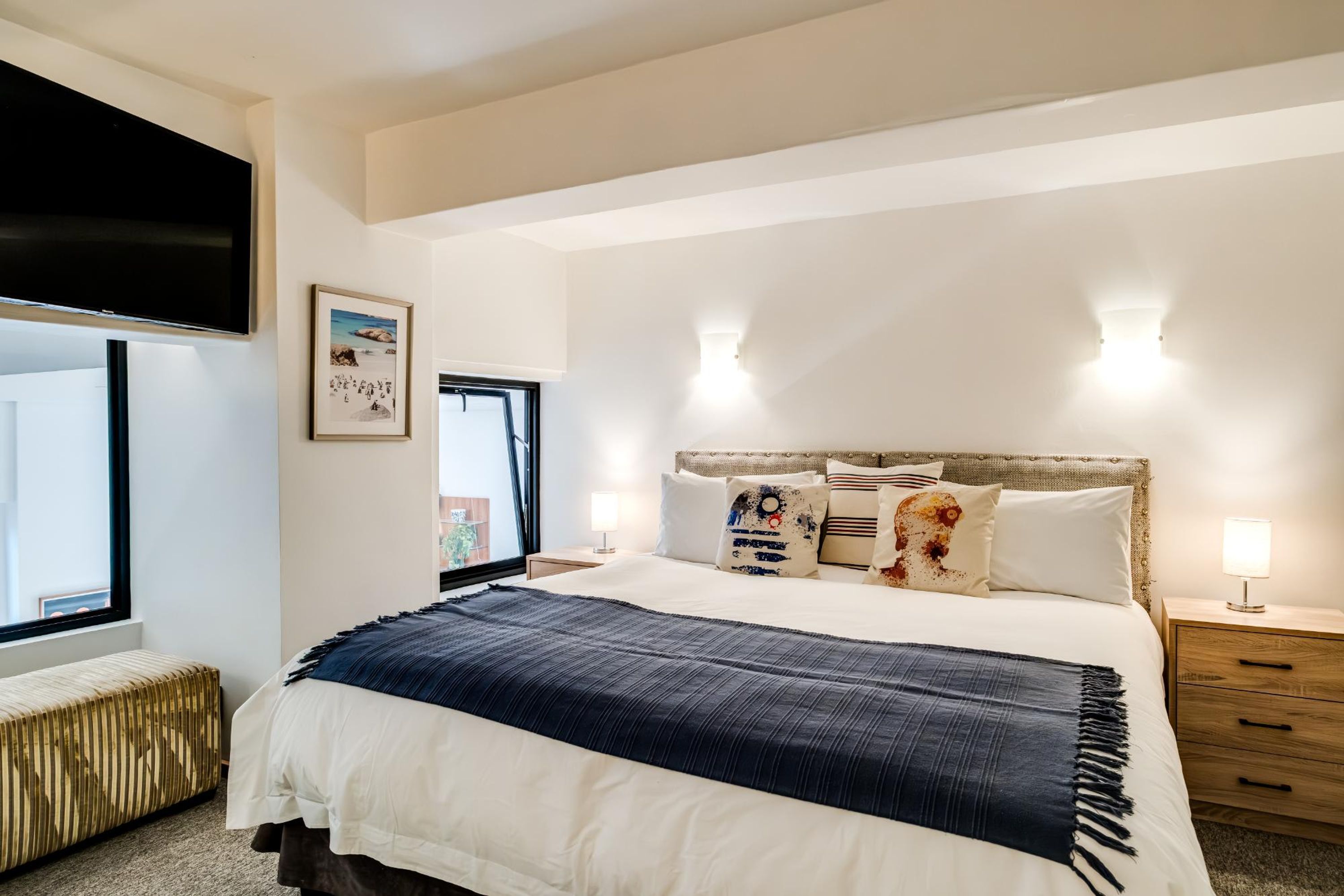 A bedroom with a large bed, bedside lamps, a window, and a wall-mounted TV.