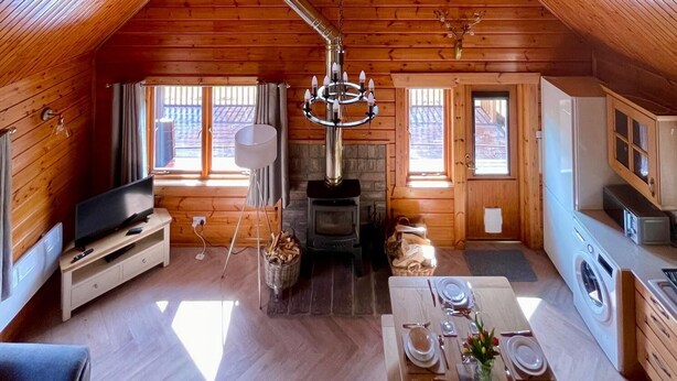 A cozy cabin with a high ceiling, wooden walls, a fireplace, a dining area, and a television. - Riverside Lodge—3-Bed Retreat in Aberdeenshire
Cozy, scenic, and peaceful. (Huntly)