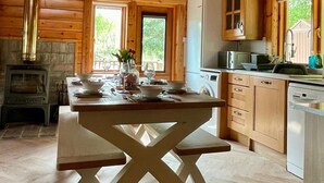 A wooden cabin interior with a dining table, kitchen area, and a fireplace. - Riverside Lodge—3-Bed Retreat in Aberdeenshire
Cozy, scenic, and peaceful. (Huntly)