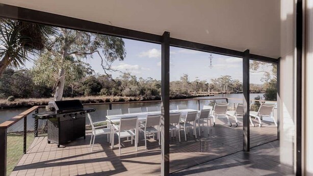 An outdoor patio with a grill, white chairs, and a view of a lake and trees.