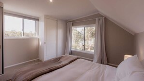 A bedroom with a large window, a bed with white bedding, and a nightstand with a lamp.