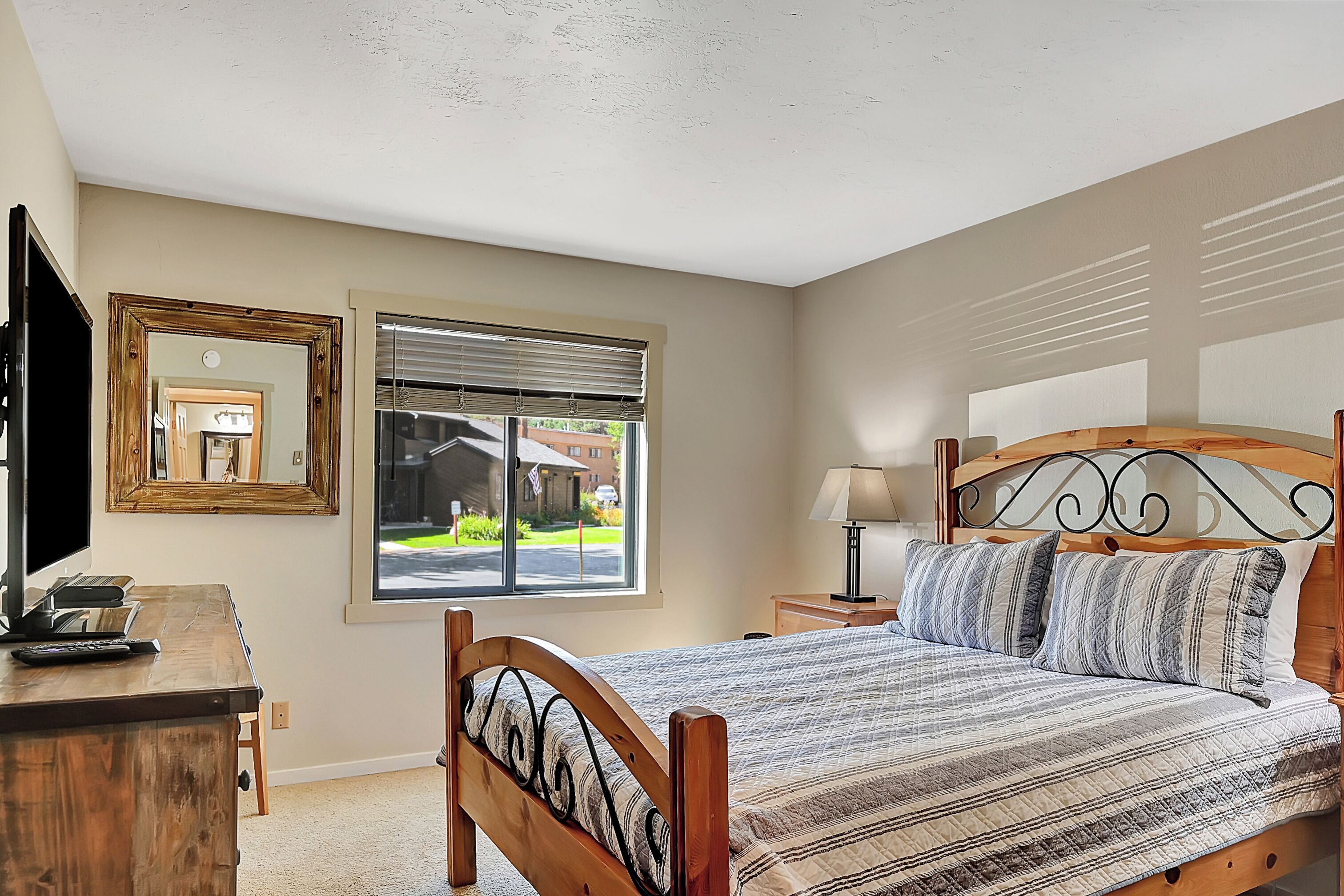Un dormitorio con una cama de madera, un escritorio, un espejo y una ventana con persianas.