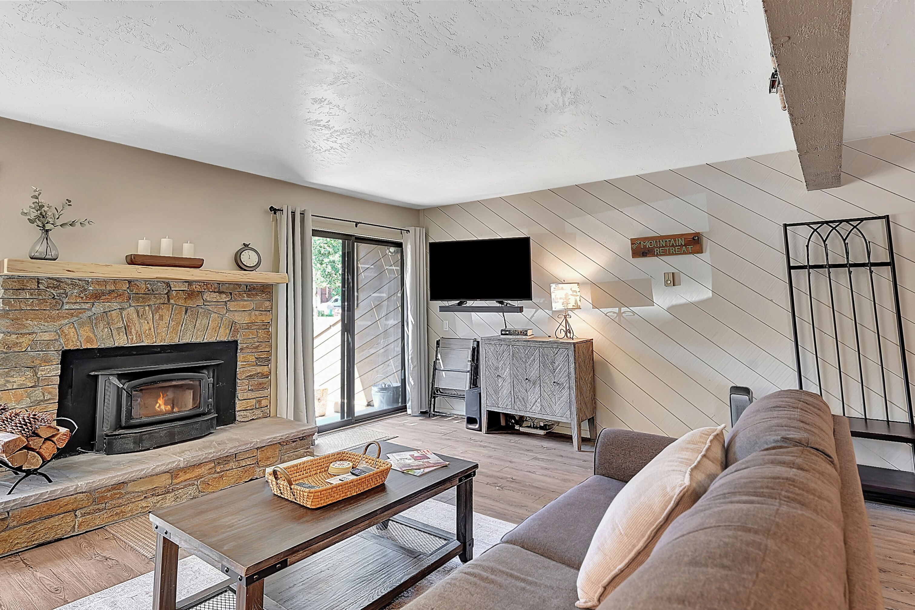 A living room with a stone fireplace, a flat-screen TV, a sofa, and a dining table.