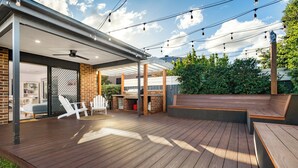 Een overdekt terras met houten vloer, een barbecuehoek en een zite hoek.