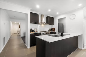 Een moderne keuken met donkere kastjes, een centraal eiland met een spoelbak en een roestvrijstalen afzuigkap.