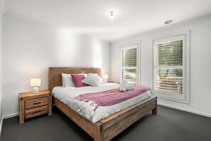 Une chambre à coucher avec un lit en bois, deux tables de chevet, une commode et une fenêtre avec des stores.