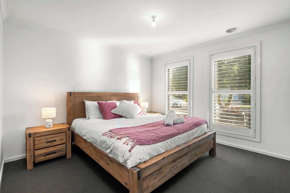 Een slaapkamer met een houten bed, twee nachtkastjes en een raam met jaloezieën.