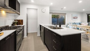 A modern kitchen with dark cabinetry, a white countertop, and a built-in dishwasher. - Family-Friendly 4BR Mount Duneed Manor (Mount Duneed)