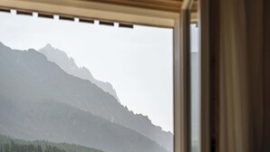 Uitzicht door een raam op een berglandschap, met een bebost gebied en een bergketen.