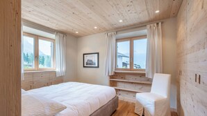 Een slaapkamer met een houten plafond, een bed, een stoel en een raam met uitzicht op de bergen.