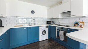 A modern kitchen with blue cabinets, a dishwasher, a microwave, and a clock on the wall. - West Hull 2 bed apartment with Parking (Hull)