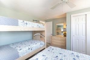 Quarto com beliche, ventoinha no teto, cômoda e uma porta.