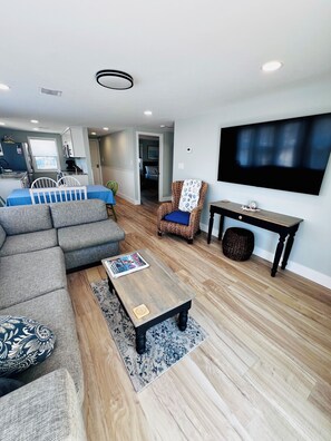 A modern living room with a sectional sofa, a patterned armchair, a coffee table, and a flat-screen TV mounted on the wall.