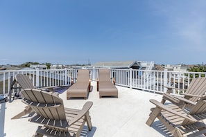 Terraço no topo do prédio com cadeiras de descanso e guarda-corpo branco.