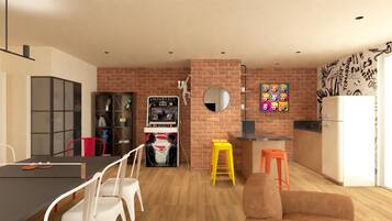 A modern kitchen with a brick wall, a refrigerator, a dining table with chairs, a bookshelf, and a gaming console.