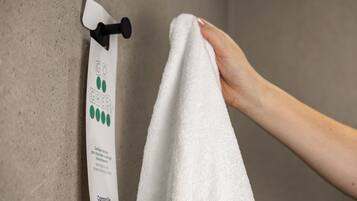 A hand holding a white towel in front of a towel dispenser with a green logo and text.