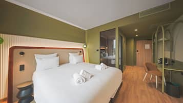A hotel room with a large bed, a sitting area, and a view into the bathroom.
