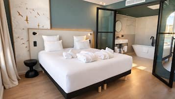 A modern hotel room with a large bed, a bathroom with a bathtub, and a glass door leading to the bathroom.