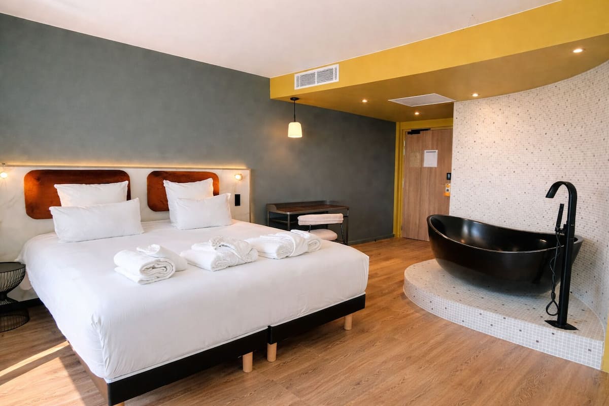 Une chambre d’hôtel moderne avec un grand lit, une baignoire noire et une petite table avec une chaise.