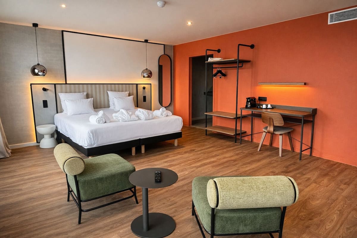 Une chambre d’hôtel avec un lit, deux chaises, un bureau, une machine à café et un miroir.