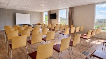 A conference room with rows of chairs, a whiteboard, a TV, and large windows with a view.