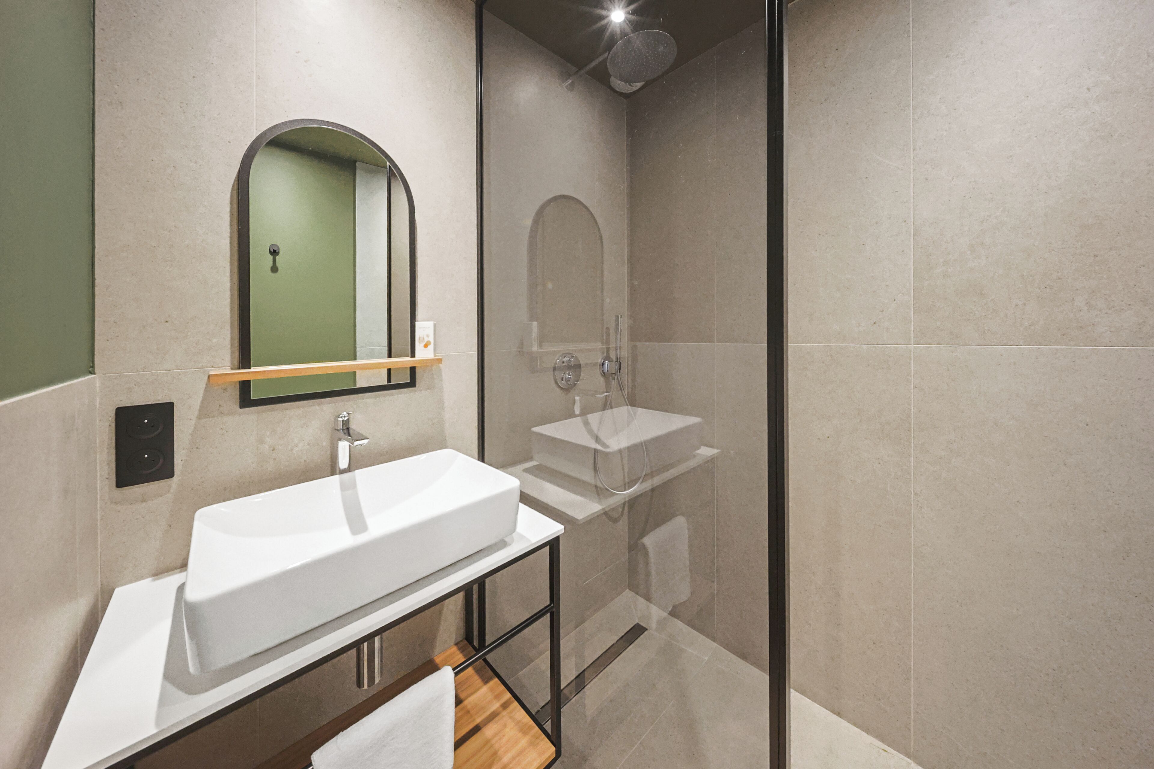 A modern bathroom with a large white sink, a mirror, and a glass-enclosed shower.