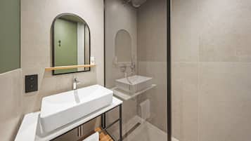 A modern bathroom with a large white sink, a mirror, and a glass-enclosed shower.