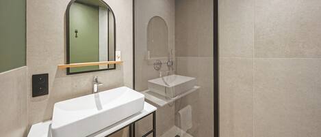 Un baño moderno con un lavamanos blanco grande, un espejo y una ducha con cerramiento de vidrio.