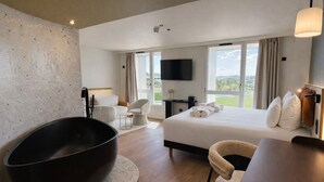 Habitación de hotel moderna con una bañera grande, una cama con toallas ordenadas, un televisor de pantalla plana y vistas al exterior.
