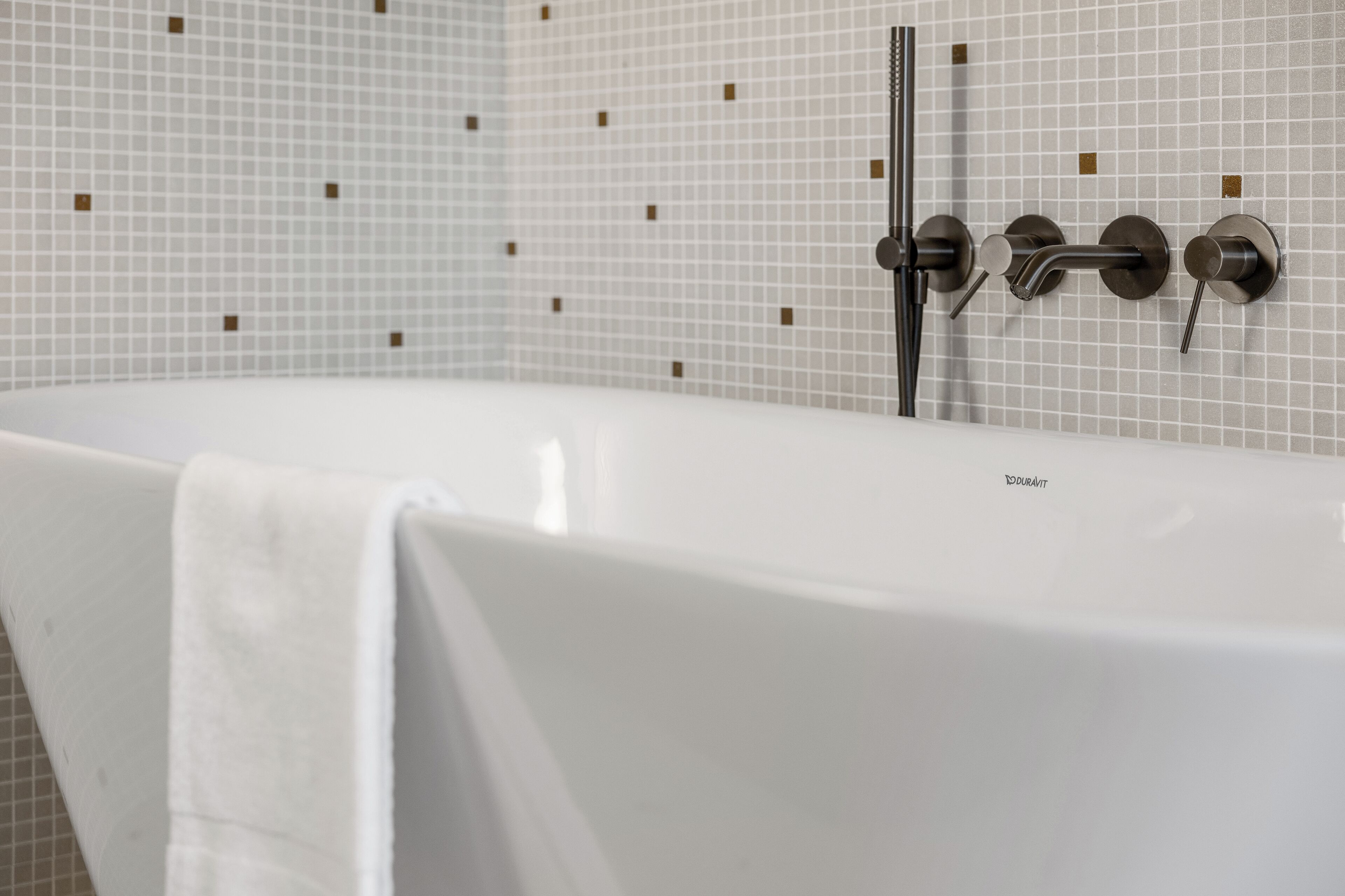 A modern bathroom with a white bathtub, a glass-enclosed shower, and a tiled wall with a geometric pattern.