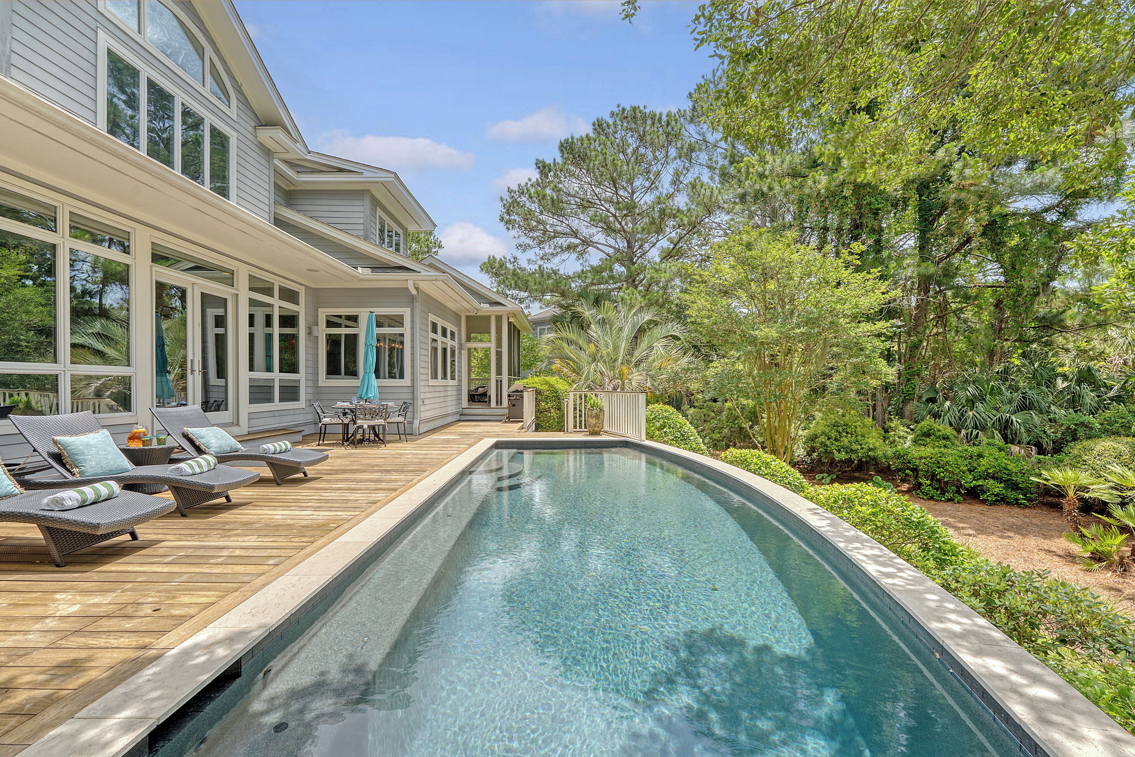 Une maison moderne dotée d’une piscine, de chaises longues et d’une végétation luxuriante.