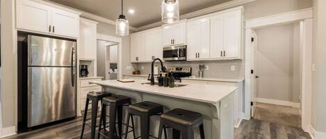 A modern kitchen with a stainless steel refrigerator, a central island with bar stools, white cabinetry, and a microwave.