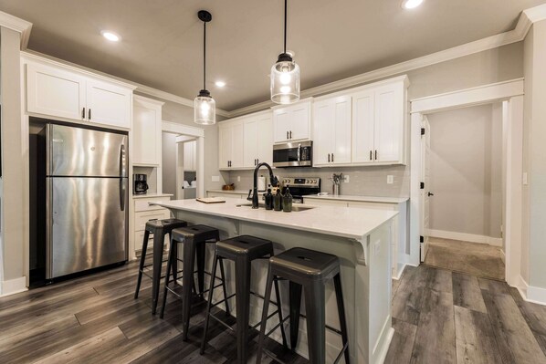 A modern kitchen with a stainless steel refrigerator, a central island with bar stools, white cabinetry, and a microwave.