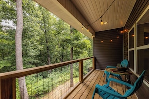A wooden deck with a railing, a table, and two chairs, overlooking a forested area.