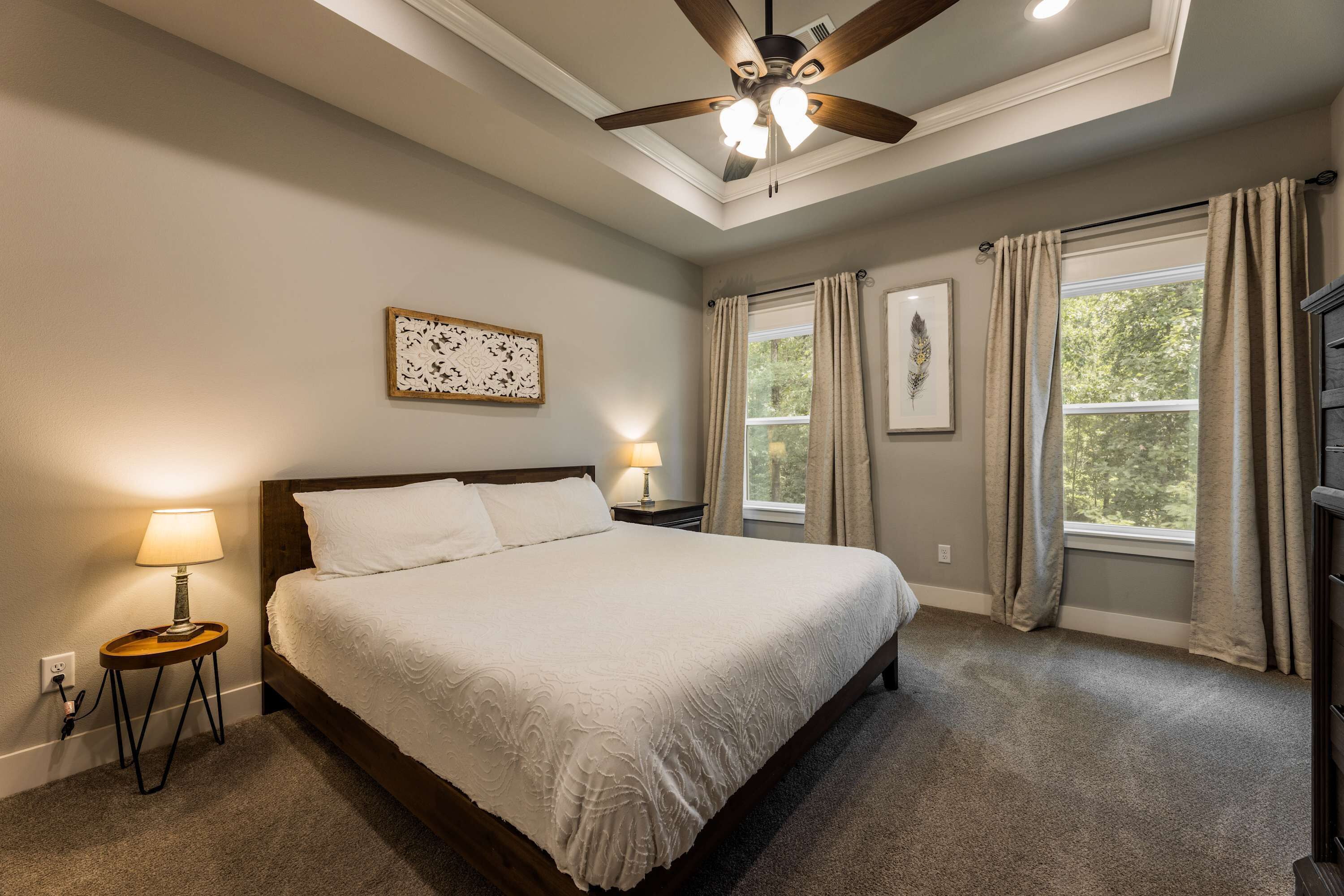 Une chambre à coucher avec un grand lit, deux lampes de chevet, un ventilateur de plafond et une fenêtre avec des rideaux.