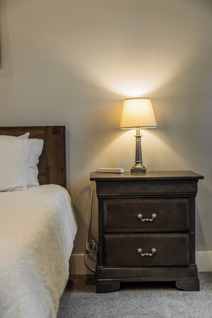 A neatly made bed with white bedding, a dark wooden nightstand with a lamp, and a wall socket. - The Abode in Bella Vista .7mi to Back 40 Trailhead (Bella Vista)