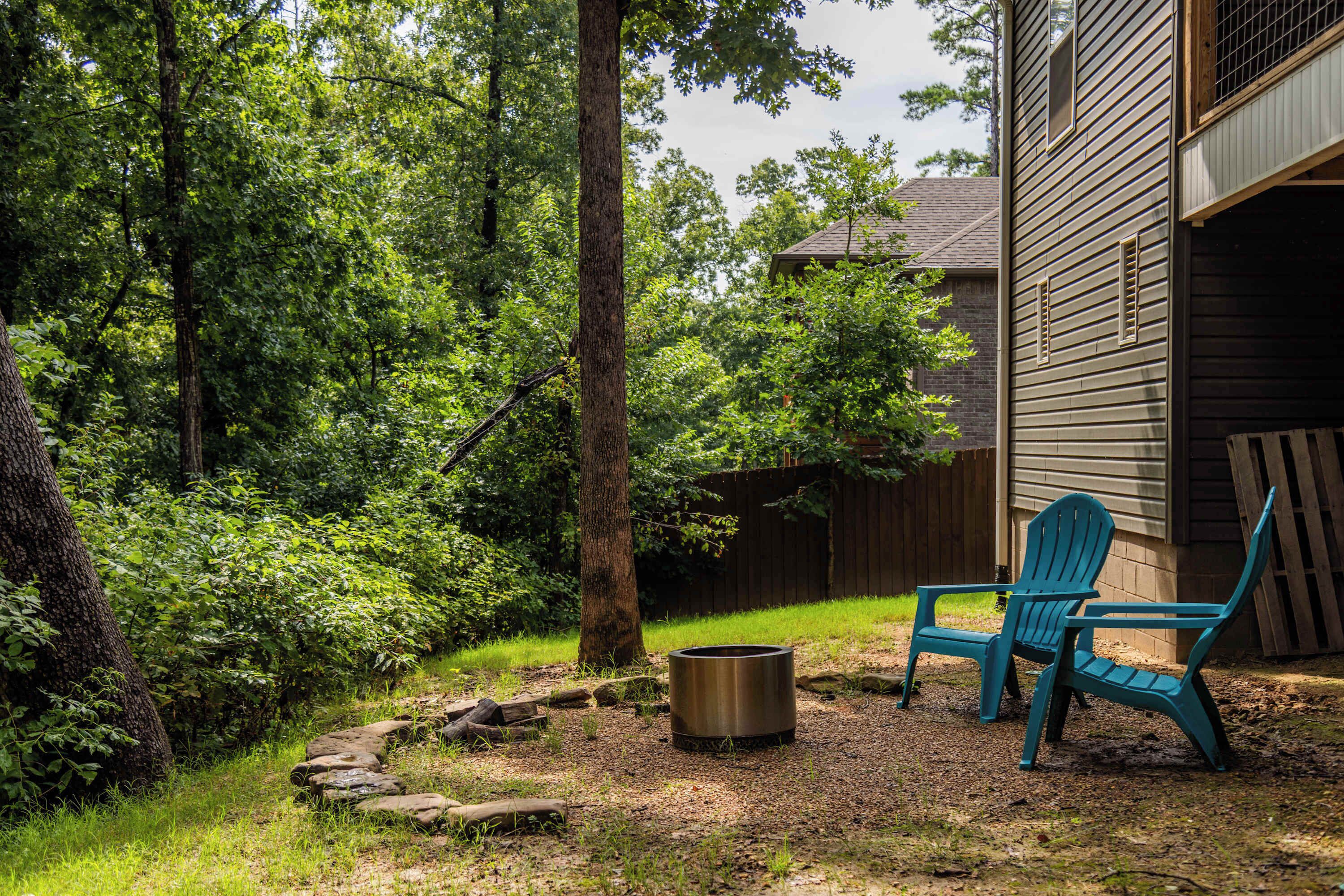 A backyard with a wooden fence, a metal fire pit, and two blue Adirondack chairs.