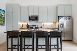Una cocina moderna con armarios grises, un refrigerador de acero inoxidable, un microondas y una barra con cuatro taburetes.