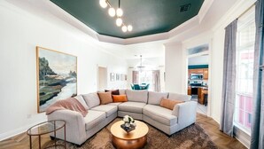 Un salon moderne avec un canapé d’angle, une table basse ronde et un tableau accroché au mur.