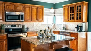 Une cuisine dotée de meubles en bois, d’appareils électroménagers en acier inoxydable, d’un plan de travail en granit et d’un îlot central avec des tabourets.