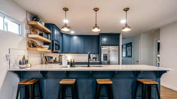 Une cuisine moderne avec des meubles de couleur bleu foncé, un grand îlot central doté de tabourets, un éclairage suspendu et un réfrigérateur en acier inoxydable.