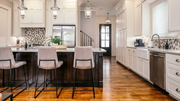 Una cocina amplia con muebles blancos, una isla central con taburetes de bar y un refrigerador de acero inoxidable.