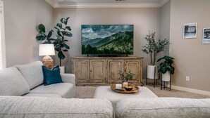 Una sala de estar con un televisor de pantalla plana, un sofá, una mesa de centro con objetos decorativos y un mueble.