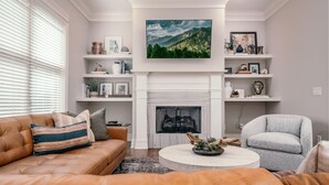 Una sala de estar con chimenea, sofás de cuero, una mesa de centro redonda y estanterías decorativas.
