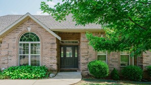 A brick house with a dark front door, a large arched window, and a small porch.